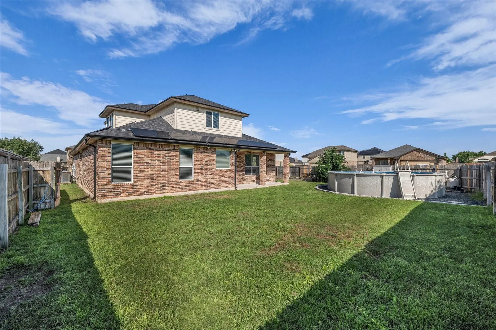 Eye-level view of a spacious backyard with a sparkling pool and covered patio in a family home
