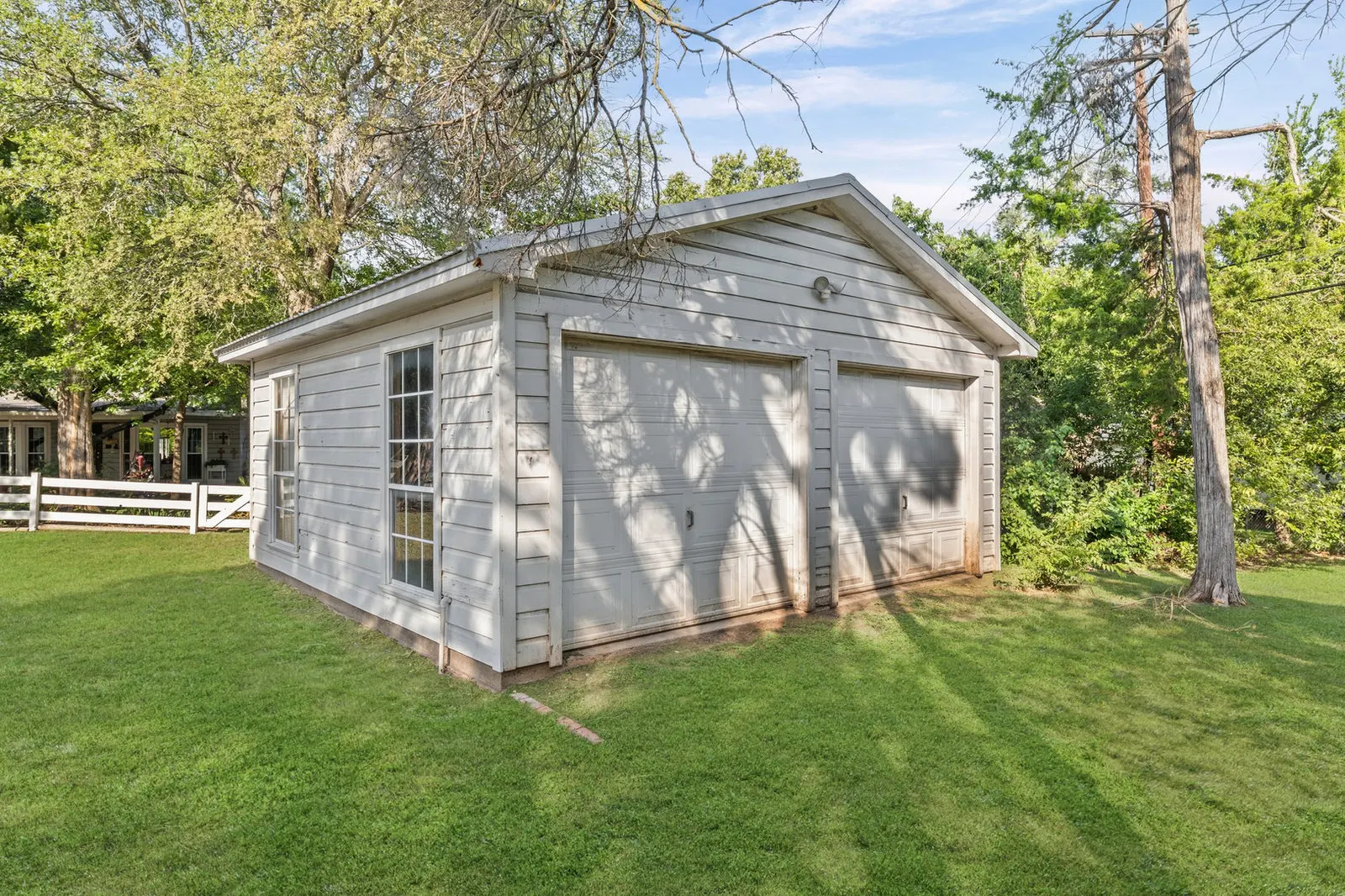 Wide-angle view of a detached workshop and garage near a spacious farmhouse yard.