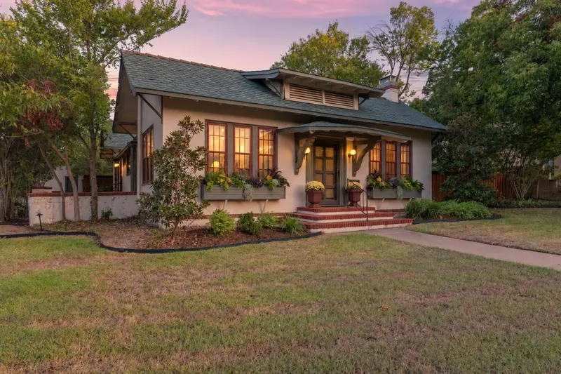 Stucco exterior with a gabled roof, prominent front porch with decorative corbels, and brick-tread steps